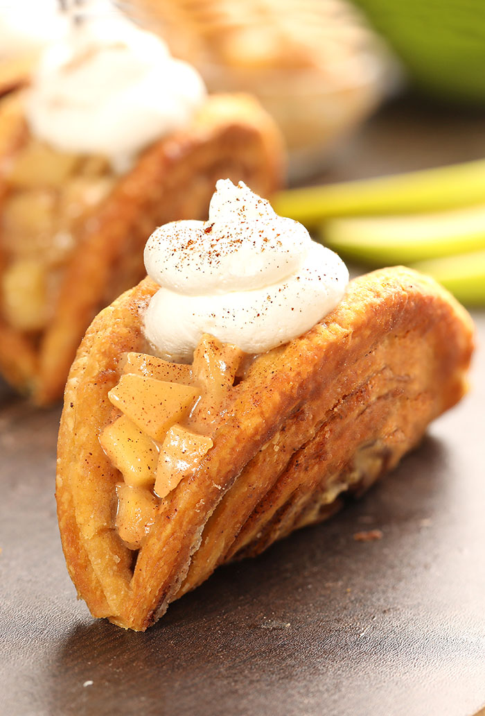 Apple Pie Cinnamon Roll Tacos - Warm, cinnamon-crusted cinnamon roll folded into a taco shape, filled with apple pie goodness, and topped with whipped cream. The most delicious apple and cinnamon taco combo EVER.