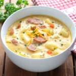 Bowl of creamy kielbasa potato soup with cheddar and parsley on a wooden table