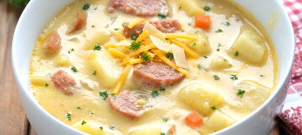 Bowl of creamy kielbasa potato soup with cheddar and parsley on a wooden table